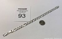 Full view of the silver Figaro bracelet laid out with a quarter coin for size comparison and a MaxSold auction card number 93.