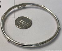 Sterling silver bangle bracelet shown next to a quarter coin for size comparison. Circular with smooth finish, clasp and hinge visible.