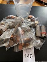 Multiple plastic bags and some coin rolls containing assorted Canadian coins of various denominations and years on a dark surface near a plastic container