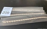 Three silver-tone metal magnetic bracelets in plastic sleeves on black surface.