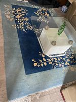 Full view of the oriental carpet showing the blue center with beige floral vines, light blue border, and some visible stains.