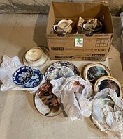 Porcelain lot packed in a cardboard box along with some items laid out on floor including plates, pitchers and figurines.