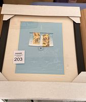 Framed commemorative postal stamp still in protective packaging, showing the full item with black frame and beige mat, photo captures the size and overall presentation of the item.
