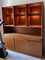 Front view of teakwood wall cabinet with upper compartments lit, showing wood grain and cabinetry details.