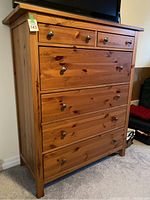 Front view of the wooden tall dresser showing five drawers with metal knob handles and a slight overhang on the top.