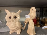 Front view of two beige glazed pottery bird figurines, owl and parrot, with lot tag attached.