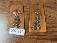 Front view of two rectangular wooden plaques with raised copper child figures sitting and standing on potty chairs.