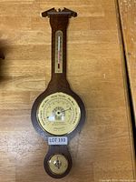 Full view of wooden barometer and thermometer showing the wood frame, brass dials, and thermometer at top.