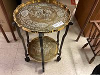 Full view of the two-tier occasional table showing etched brass trays and wood folding legs with casters.