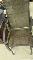 Close-up photo of the brown gliding outdoor chair showing the mesh fabric seat and backrest with metal frame.