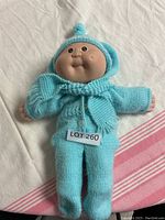 Full doll showing blue knitted hooded sweater, pants, and hat with pom-pom.