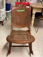 Front view of the child’s folding rocking chair showing carved top and cane seat and backrest.
