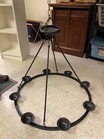Black metal hanging outdoor fixture placed on a basement floor, showing circular design and candle holders.