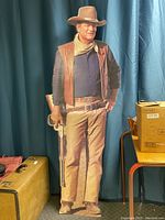 Full view of life size cardboard cutout of John Wayne in western attire holding a rifle.