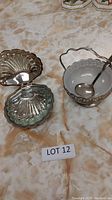 Photo of clam shell shaped silver plated dish with removable glass insert on a table with marble-like surface.