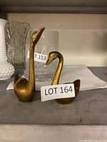 Pair of brass swan figurines on a shelf, showing front and side profile.