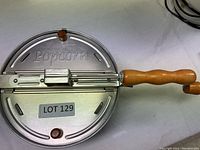 Top view of metal popcorn maker lid with 'Popcorn' embossed and wooden knob