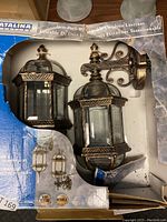 Twin pack of bronze-finished outdoor lanterns visible in original box with branding and condition shown