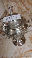 Silver spoon holder showing full body, hooks, lid with decorative handle, and pedestal base.