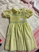 Full view of yellow child's smocked dress with puff sleeves and Peter Pan collar.