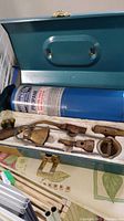 Opened metal case showing propane canister and soldering attachments in foam insert.