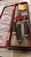 Photo of the carving set inside the open box, showing the knife, fork, and sharpening steel with antler handles and metal blades.
