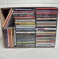 Box containing 50 assorted compact disc jewel case CDs stacked compactly in three rows showing various album spines and some front covers.