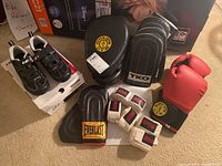 Photo showing Louis Garneau cycling shoes on top of white shoe box, red Gold's Gym boxing gloves, black curved training pads labeled Gold's Gym and TKO, and white Boes hand wraps arranged in front.
