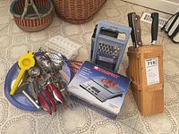 Photo showing overall lot with butcher block and knives, kitchen utensils pile including graters, juicer, ice cube trays, pizza cutter and more.