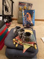 Photo of camping lot contents showing blue cushions, metal mugs wrapped in plastic, colorful Southwestern quilt or blanket, boxed inflatable boat, yellow lanterns, and several batteries.