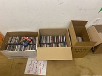 Three cardboard boxes filled with assorted music CDs, showing the variety and quantity in the lot.