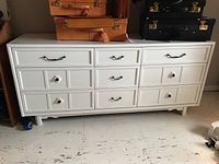 Front view of white painted oak dresser with nine drawers, metal bail pulls and ceramic knobs.