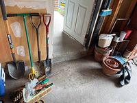 Photo showing garden tools including shovel, spade, garden fork, and hand tools leaning against wall