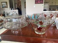 Wide shot showing the glass cake plate with cover and the chip and dip bowl on a wooden table with living room background.
