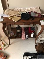 Wide view of vintage gloves, purses, ties and accessories on a wooden table and lower shelf with a lantern and other small objects.