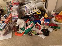 Overview of mixed household tools, hardware, light bulbs, and batteries spread on carpeted floor.