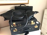 Four black leather luggage pieces stacked showing handles and locks