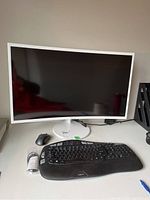 Front view of white curved monitor powered off, Logitech keyboard and mouse on desk.