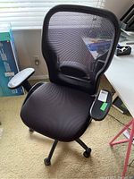 Front angled view of black office chair showing seat, armrests, and caster wheels, with minor damage visible on left armrest.