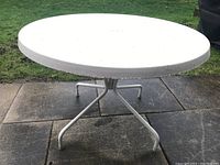 Full view of the round white fiberglass tabletop with metal legs, showing the table outdoors on a concrete patio.