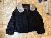 Full view of the black Persian lamb fur jacket with light brown mink collar laid flat.