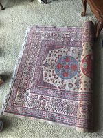Partially rolled Persian wool rug on carpeted floor, showing detailed edge and fringes.