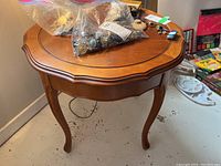 Wood side table with curved legs and scalloped edges, scratches on surface, with various small bags on top