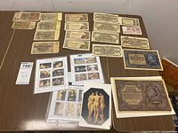 Table displaying a collection of vintage banknotes, several sheets of postage stamps, and art postcards depicting Renaissance paintings.