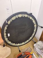 Mini trampoline viewed from underside showing metal frame, springs partially covered with padding, and four legs with black caps.