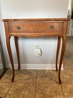 Front view of vintage wooden hall table showing drawer and curved legs, against white wall with outlet.