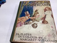 Front cover of the vintage Alice in Wonderland book with illustrated characters and title text.