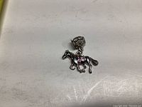 Photo showing silver-tone dangling horse charm with jump ring and clasp on plain background.