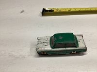 Top view of green and white diecast Triumph toy car with measuring tape showing length approximate 3.25 inches. Paint is heavily worn and chipped on roof and hood.