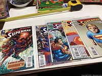 Five Superman comic books laid out on a table, showing cover art and titles, individually bagged